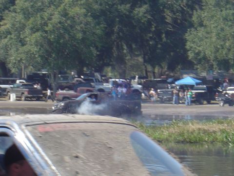1987 Suzuki Samurai - Multiple trucks participate in a mud bogging event, with one vehicle stuck in the mud and emitting smoke.