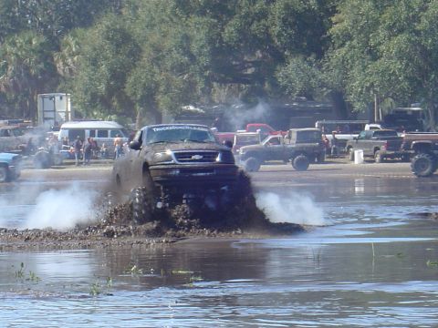 1987 Suzuki Samurai - A lifted truck powers through a mud bog, creating a large spray of water and dirt.