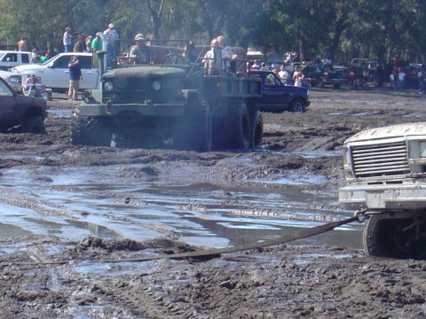 1987 Suzuki Samurai - A military truck is stuck in a muddy field, with another vehicle attempting to tow it out.