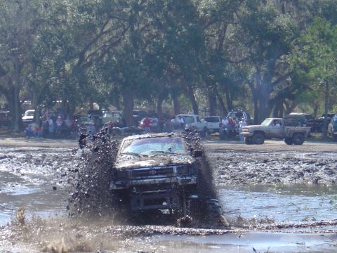 1987 Suzuki Samurai - A truck navigates a muddy obstacle course with spectators watching.