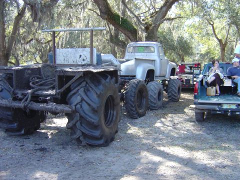 1987 Suzuki Samurai - A heavily modified truck with oversized tires sits in a wooded area next to another pickup truck.