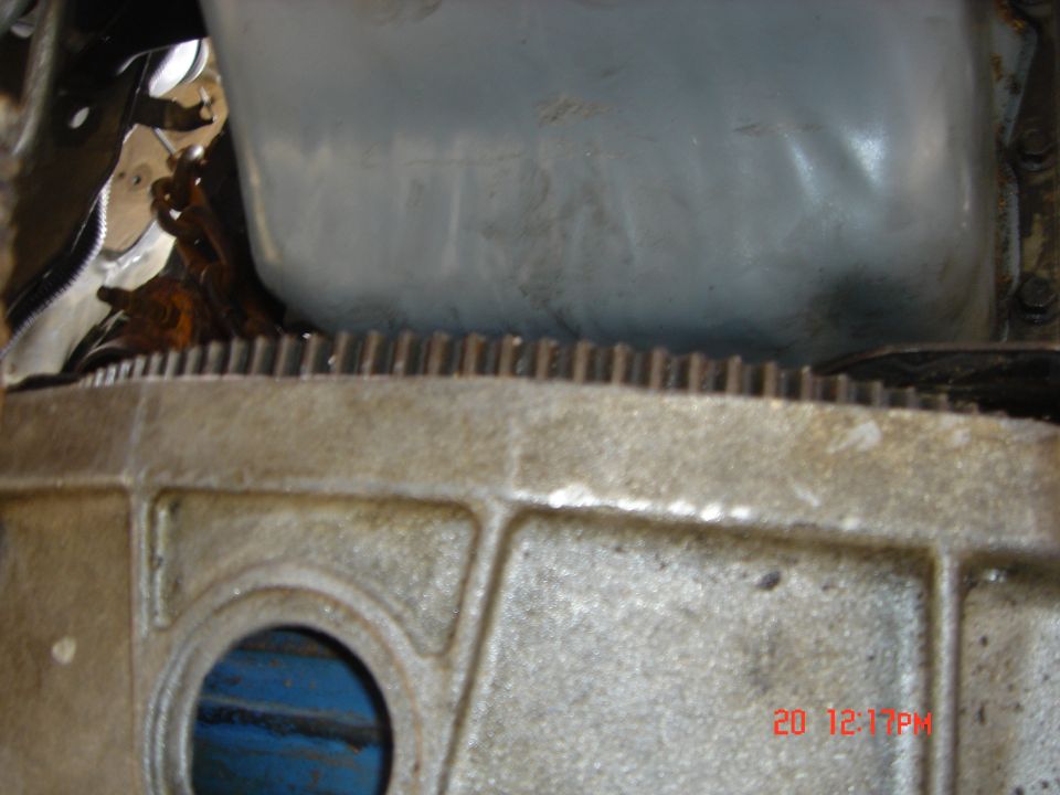 Aluminum bellhousing and flywheel ring gear teeth with blue engine block visible through inspection port
