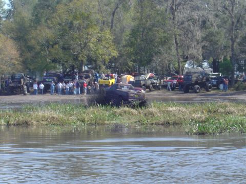 1987 Suzuki Samurai - Trucks churn up mud and water during a competition while onlookers observe from the shore.