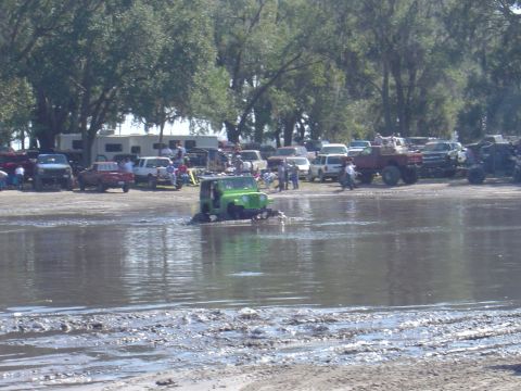1987 Suzuki Samurai - A green Jeep Wrangler navigates a muddy, water-filled area with spectators and other vehicles present.