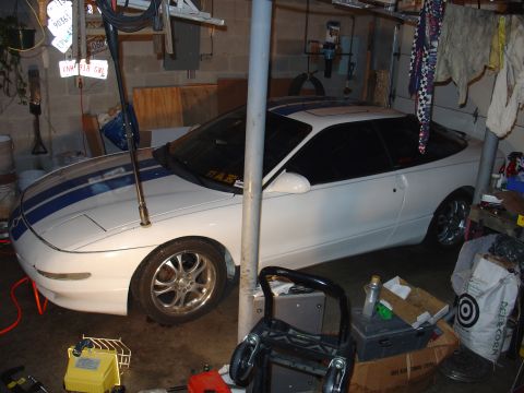 1993 Ford Probe - A white 1993 Ford Probe coupe with blue racing stripes is parked in a cluttered garage.