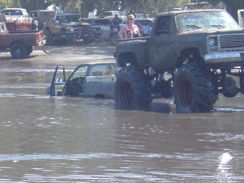 1987 Suzuki Samurai - Mud bog event with a monster truck and a submerged pickup truck.