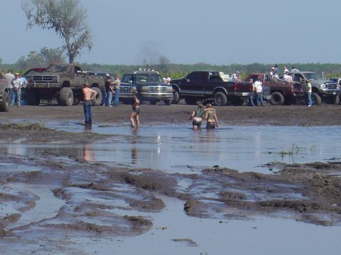 1987 Suzuki Samurai - People and trucks gather in a muddy field, with some wading in the water.
