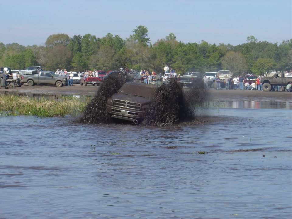 Front view of a mud-covered 1994 Dodge Ram truck splashing through a mud bog