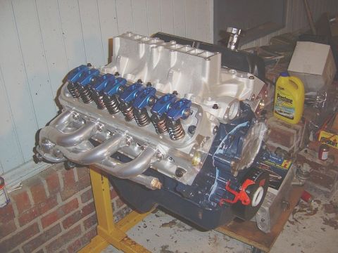 1986 Ford Bronco - V8 engine with aftermarket intake and headers, on an engine stand. A bottle of Prestone is nearby.