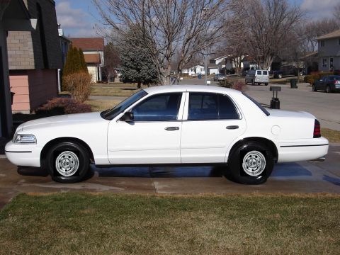 2000 Ford Crown Victoria - A white sedan is parked on a concrete driveway in front of a residential house.