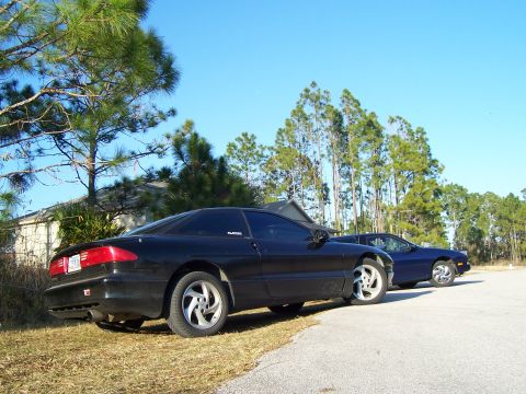 1994 Ford Probe - Two Ford Probes are parked on a sunny day with trees and a house in the background.