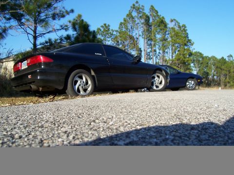 1994 Ford Probe - Two Ford Probe cars are parked side-by-side on a gravel lot with trees in the background.