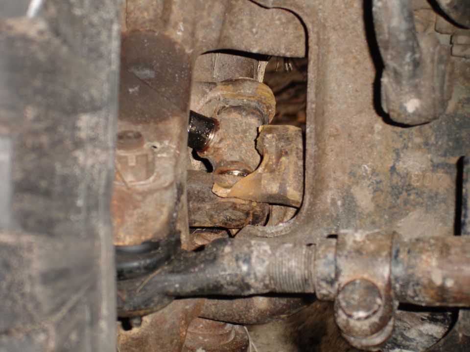 Close-up of a broken suspension component, possibly a ball joint or tie rod end, showing rust and damage