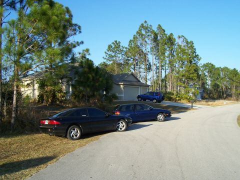 1994 Ford Probe - Two cars are parked in front of a suburban house on a sunny day.