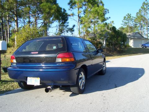 1994 Ford Probe - A blue hatchback with a custom exhaust pipe is parked on a street in front of a house.
