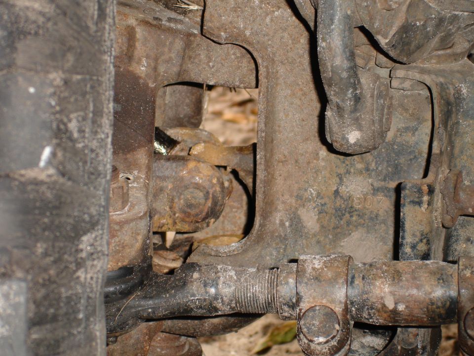 Close-up of rusty suspension parts, possibly from a truck or SUV. Some numbers are visible on a metal bracket