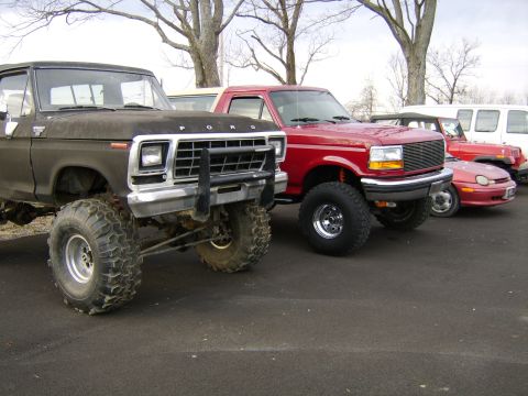 1978 Ford Bronco - Two lifted Ford trucks are parked side-by-side, with other vehicles in the background.