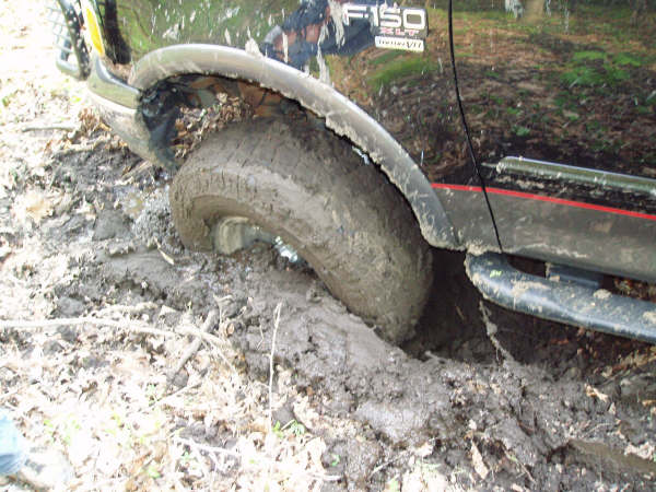 Black Ford pickup front wheel buried in deep mud, tire and fender coated in mud, F-150 badge visible