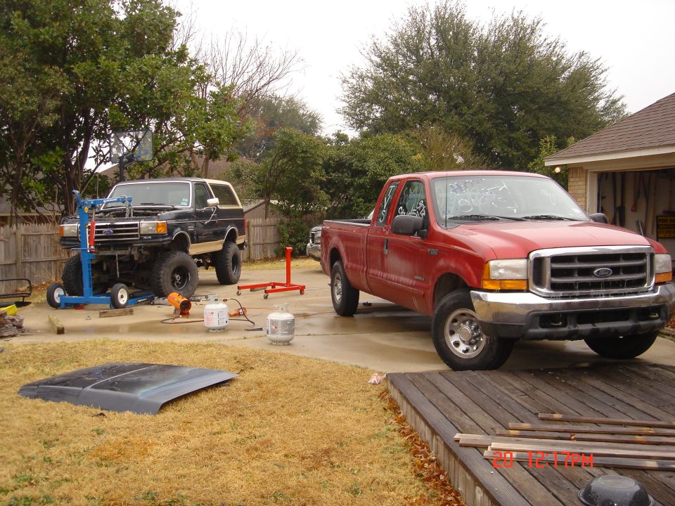 Black Ford Bronco with engine hoist, red Ford pickup truck parked nearby, hood on the grass