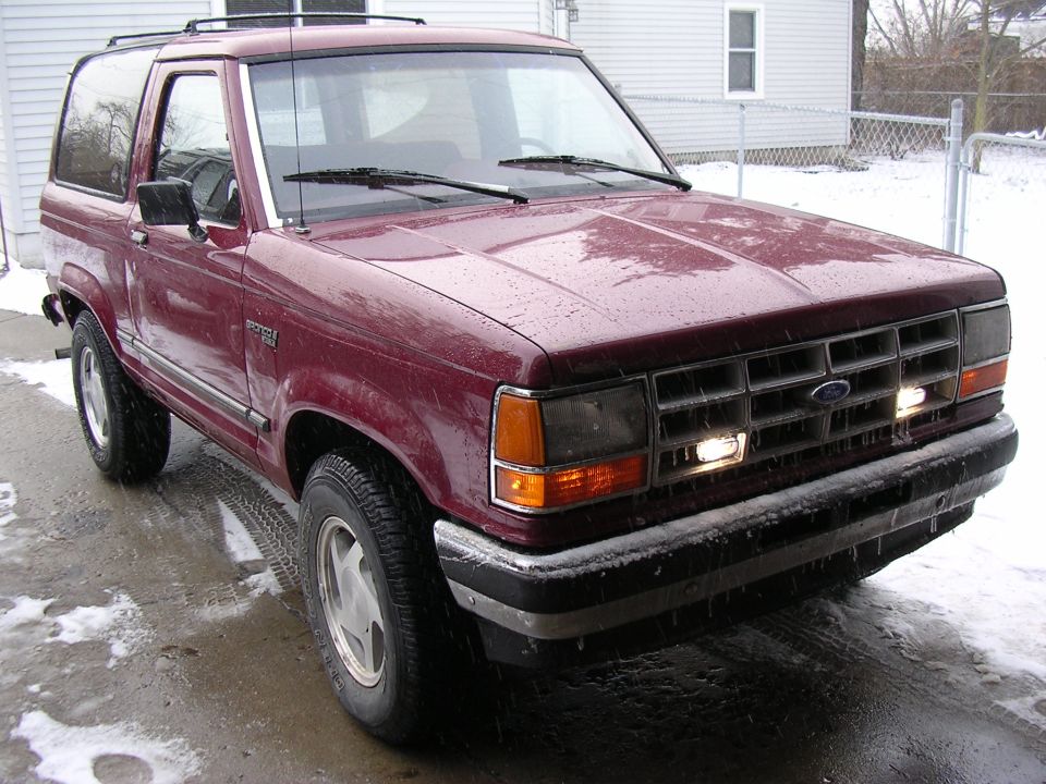 Maroon Ford Bronco II three-quarter front view on snowy driveway with lights on