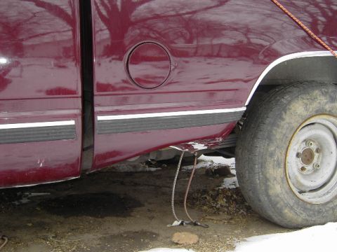 1997 Chevrolet C/K Pickup - The side of a maroon 1997 Chevrolet C/K Pickup truck is visible, including the fuel door and rear wheel.