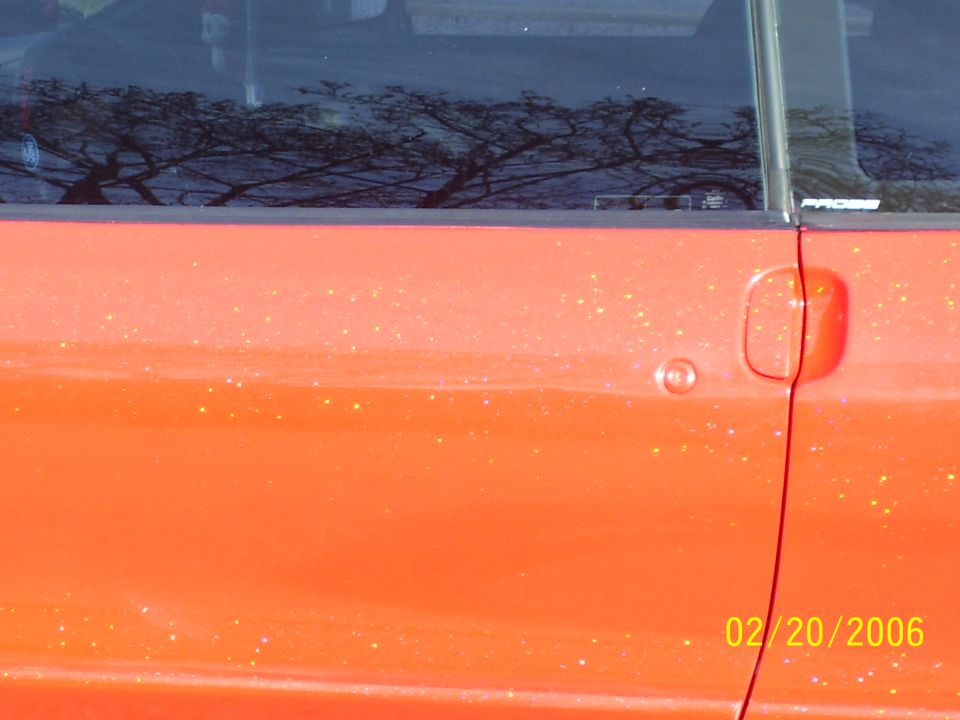 Close-up of orange metalflake paint on a car door with handle and reflective glass, dated 2006