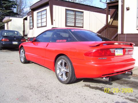 1994 Ford Probe - A red 1994 Ford Probe is parked next to a trailer home, with a dark sedan visible behind it.