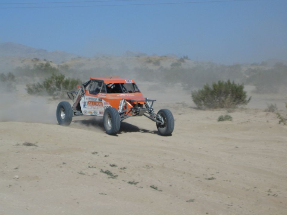 Orange and white off-road race buggy on a desert trail under blue sky