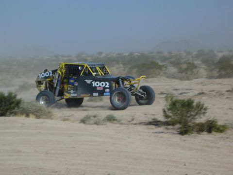 Black off-road race buggy number 1002 speeding through desert dust