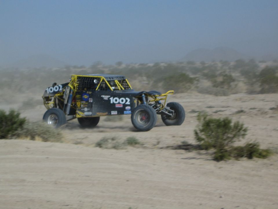 Black off-road race buggy number 1002 speeding through desert dust