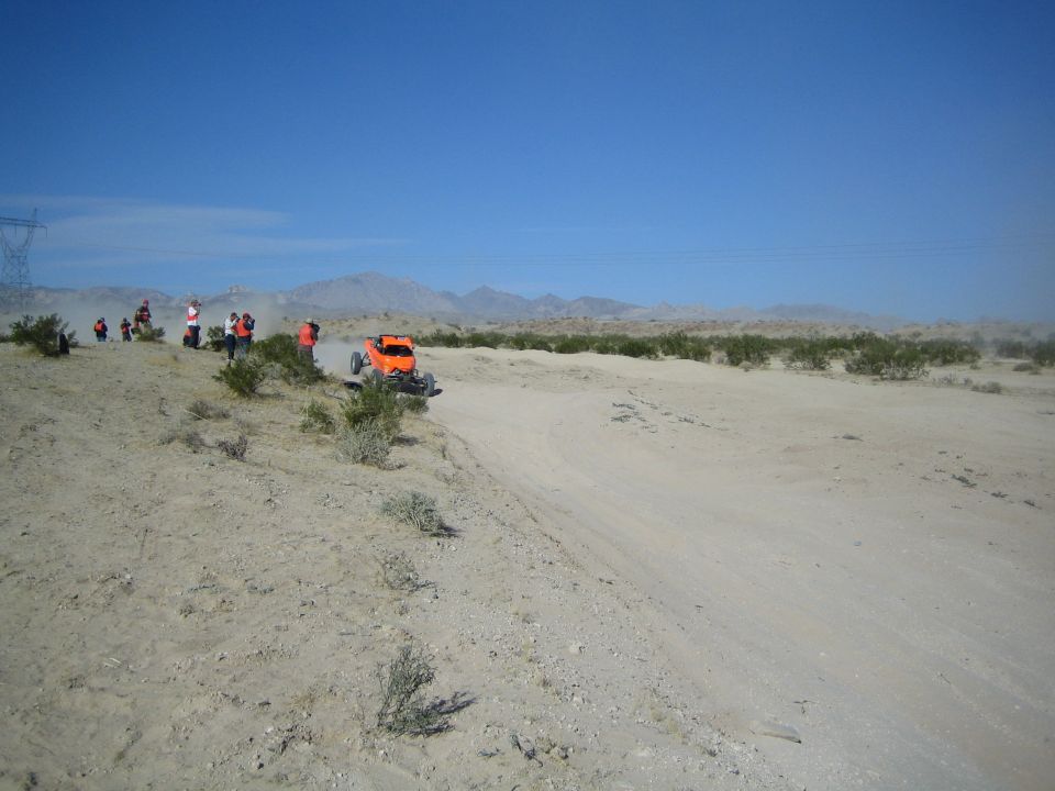 Orange off-road buggy passing spectators on a desert course