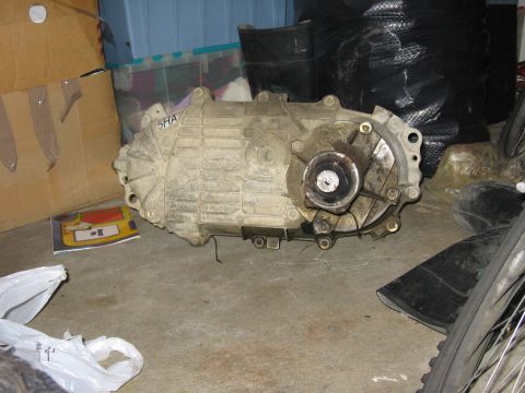 1987 Ford Bronco - A transfer case, possibly from a Ford F-150, is shown in a storage area. The part has a visible marking of '5HA'.