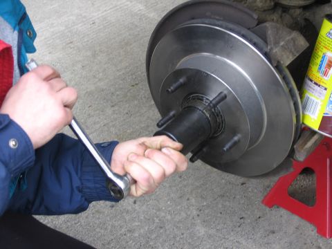 1987 Ford Bronco - A person uses a wrench on a vehicle's brake rotor and hub assembly, supported by a red jack stand.