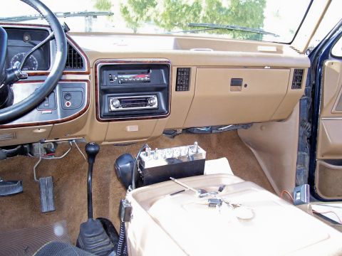 1991 Ford Bronco - Interior view of a tan dashboard and center console, showing a manual transmission shifter and aftermarket radios.