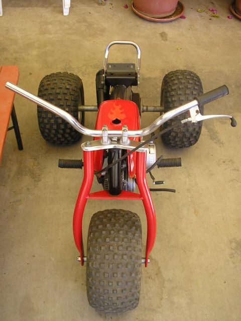 1900 Honda Big Red - This three-wheeled ATV is parked on a concrete surface, with a wooden table to the left.