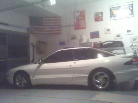 1996 Ford Probe - A white 1996 Ford Probe is parked inside a garage, with posters and an American flag visible on the wall.