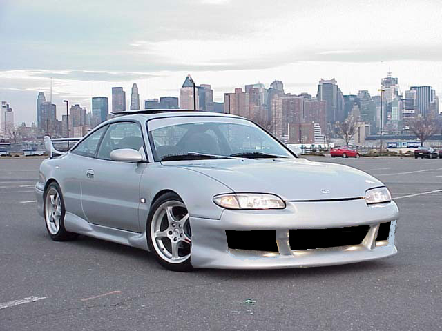Silver coupe with aftermarket body kit and spoiler, city skyline in background