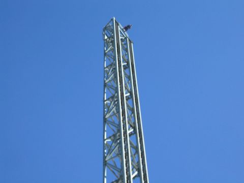 1990 Ford Bronco - tall silver steel-lattice amusement park tower ride rises against a clear blue sky with a small object at the top.