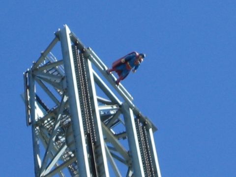 1990 Ford Bronco - costumed Superman figure is mounted near the top of a silver steel-lattice tower ride against a blue sky.