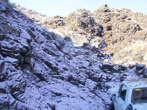 1978 Ford Bronco - A white pickup truck navigates a snowy mountain path, with rocky terrain and sparse vegetation visible.