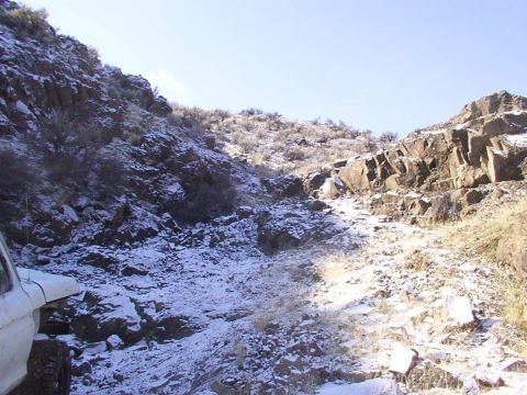 1978 Ford Bronco - A snowy mountain trail with a vehicle partially visible on the left side.