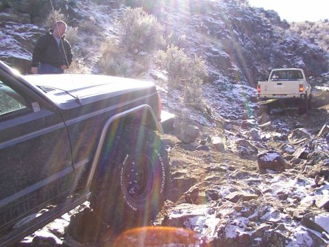 1978 Ford Bronco - Two off-road vehicles navigate a challenging, rocky terrain with patches of snow under a bright sun.