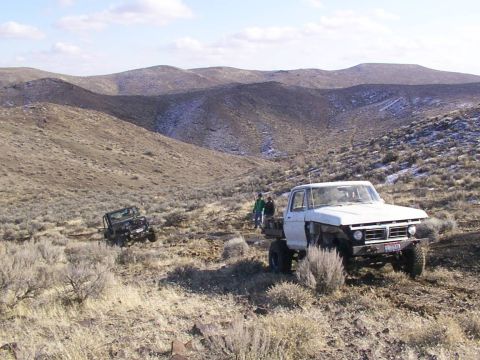 1978 Ford Bronco - A white SUV is parked on a dry, rocky slope, with hills stretching out behind it under a clear sky.