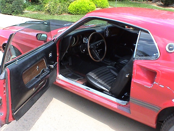 Open door of a red Mustang showing black bucket seats, dash and steering wheel; pony on door panel