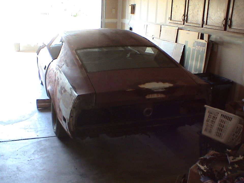 Rear three-quarter of a dusty primer fastback project car stored in a cluttered garage
