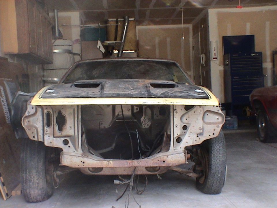 Front view of a stripped primer fastback shell with twin hood scoops and no engine, in a garage