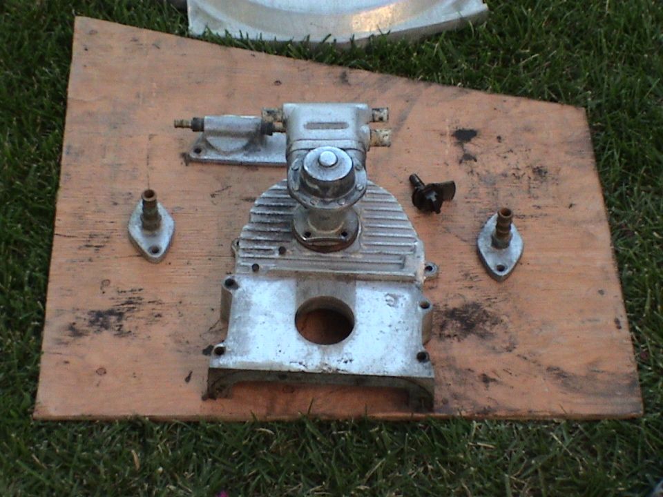 Mechanical assembly with valve cover and two mounting flanges set on a wooden board in grass