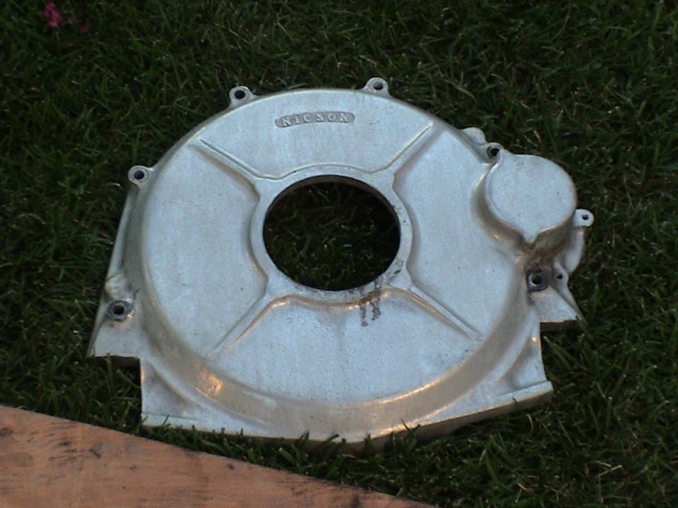 Cast aluminum bellhousing or flywheel cover lying face up in grass with a large center hole
