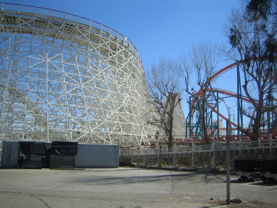 White wooden roller coaster structure beside a red steel coaster under blue sky
