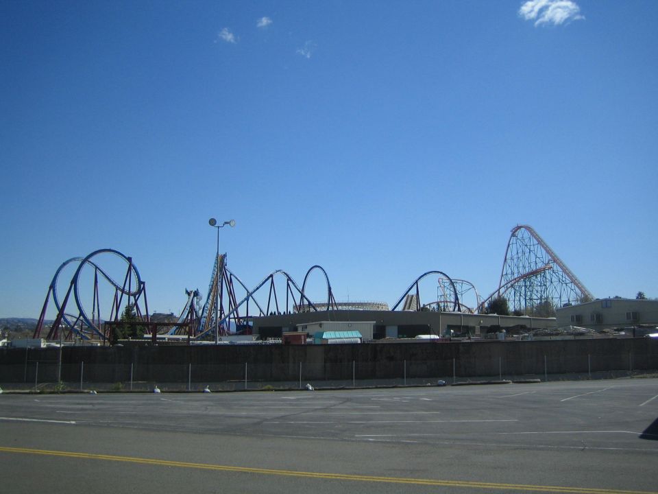 Distant amusement park skyline of multiple roller coasters behind a fenced lot